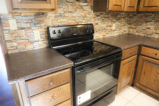 3823 N Harvard Ave Unit 12, Oklahoma City, OK 73122 - kitchen with black range with electric cooktop, brown cabinetry, light tile patterned floors, and dark countertops