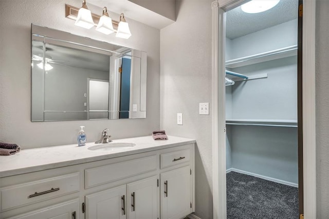 1713 Shadow Ct, Edmond, OK 73013 - bathroom featuring vanity, ceiling fan, a walk in closet, and a textured wall