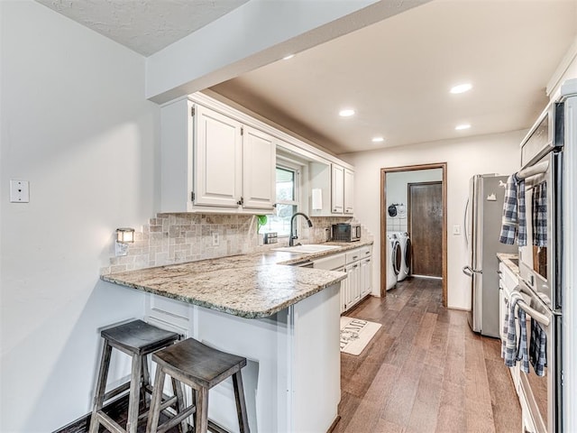 8001 84th St, Noble, OK 73068 - kitchen featuring stainless steel appliances, a peninsula, white cabinetry, decorative backsplash, and wood finished floors