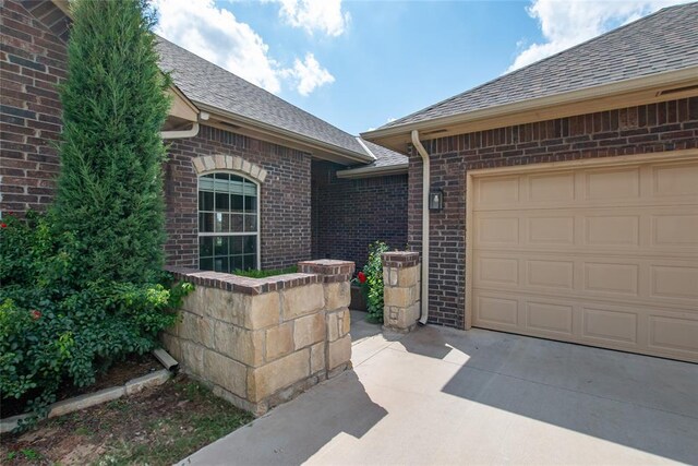 12037 Ashford Dr, Yukon, OK 73099 - doorway to property featuring driveway, brick siding, roof with shingles, and a garage