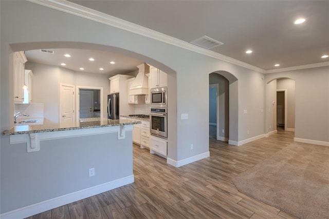 12037 Ashford Dr, Yukon, OK 73099 - kitchen with stainless steel appliances, a kitchen breakfast bar, ornamental molding, custom exhaust hood, and white cabinets