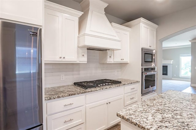 12037 Ashford Dr, Yukon, OK 73099 - kitchen with stainless steel appliances, custom exhaust hood, arched walkways, white cabinets, and ornamental molding