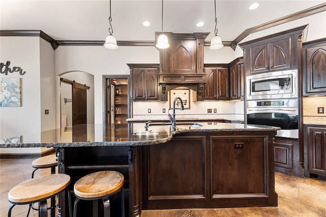 126 Castle Gate Dr, Choctaw, OK 73020 - kitchen with stainless steel appliances, ornamental molding, a barn door, an island with sink, and dark brown cabinetry