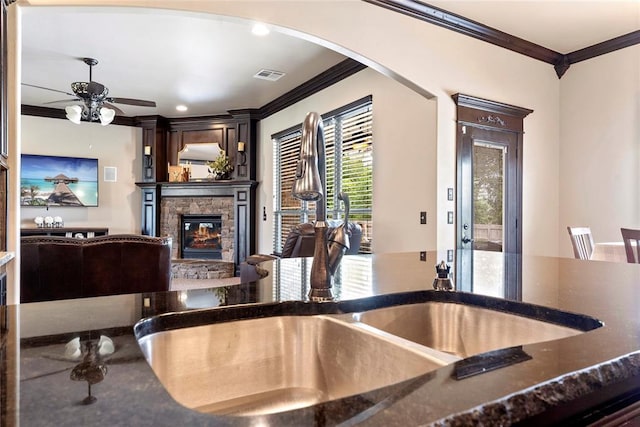 126 Castle Gate Dr, Choctaw, OK 73020 - kitchen with crown molding, arched walkways, a stone fireplace, ceiling fan, and dark stone counters
