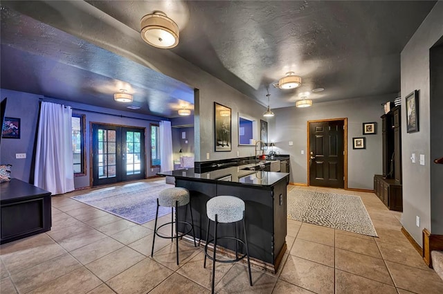 10035 Stone Gate Way, Arcadia, OK 73007 - kitchen with dark countertops, light tile patterned flooring, a peninsula, a kitchen breakfast bar, and a textured ceiling