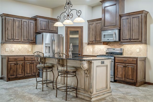 2216 SW 117th St, Oklahoma City, OK 73170 - kitchen with appliances with stainless steel finishes, a kitchen island with sink, backsplash, dark stone counters, and hanging light fixtures