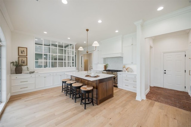 305 Carmel Valley Way, Edmond, OK 73025 - kitchen with high end range, light wood-type flooring, white cabinetry, an island with sink, and a kitchen breakfast bar