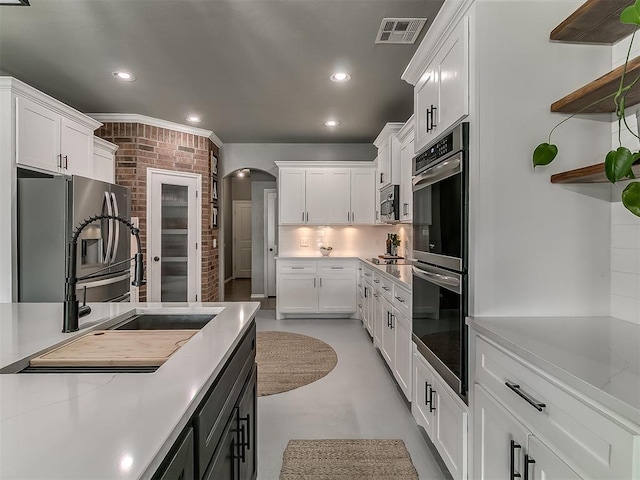 7821 Lindsay Ln, Edmond, OK 73025 - kitchen featuring appliances with stainless steel finishes, finished concrete flooring, white cabinetry, arched walkways, and recessed lighting