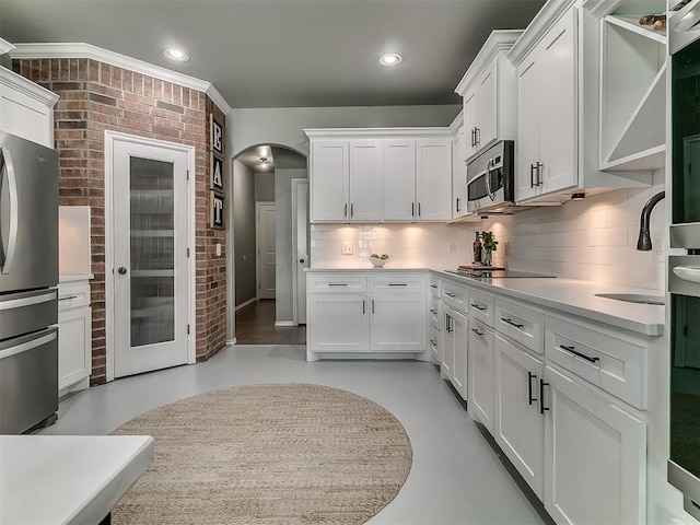 7821 Lindsay Ln, Edmond, OK 73025 - kitchen featuring stainless steel appliances, decorative backsplash, white cabinetry, arched walkways, and light countertops