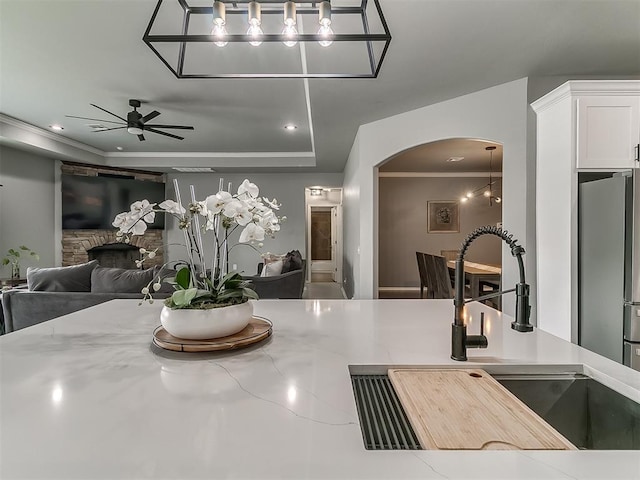 7821 Lindsay Ln, Edmond, OK 73025 - dining space featuring arched walkways, a ceiling fan, a stone fireplace, a tray ceiling, and crown molding