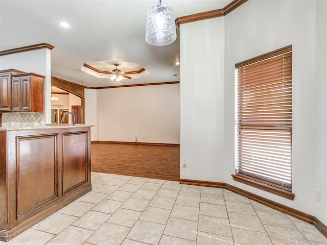 17104 Wales Green Ave, Edmond, OK 73012 - kitchen featuring crown molding, a ceiling fan, light countertops, light tile patterned floors, and backsplash