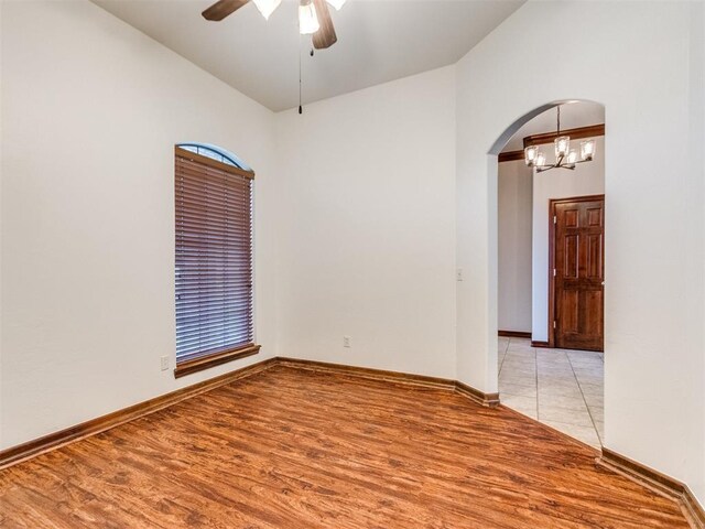 17104 Wales Green Ave, Edmond, OK 73012 - spare room with vaulted ceiling, arched walkways, a ceiling fan, light wood-style floors, and a chandelier