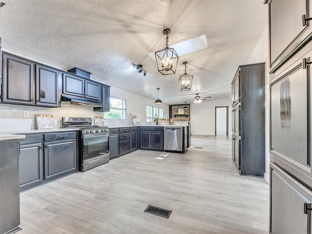 9200 Hollow Rd, Newalla, OK 74857 - kitchen featuring appliances with stainless steel finishes, a chandelier, a peninsula, light wood finished floors, and a textured ceiling