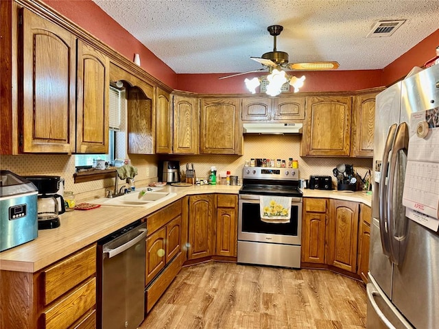 311 Parker St, Waurika, OK 73573 - kitchen with stainless steel appliances, under cabinet range hood, brown cabinets, and a textured ceiling