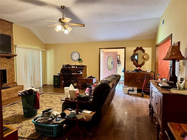 311 Parker St, Waurika, OK 73573 - living room featuring lofted ceiling, ceiling fan, wood finished floors, a textured ceiling, and a brick fireplace