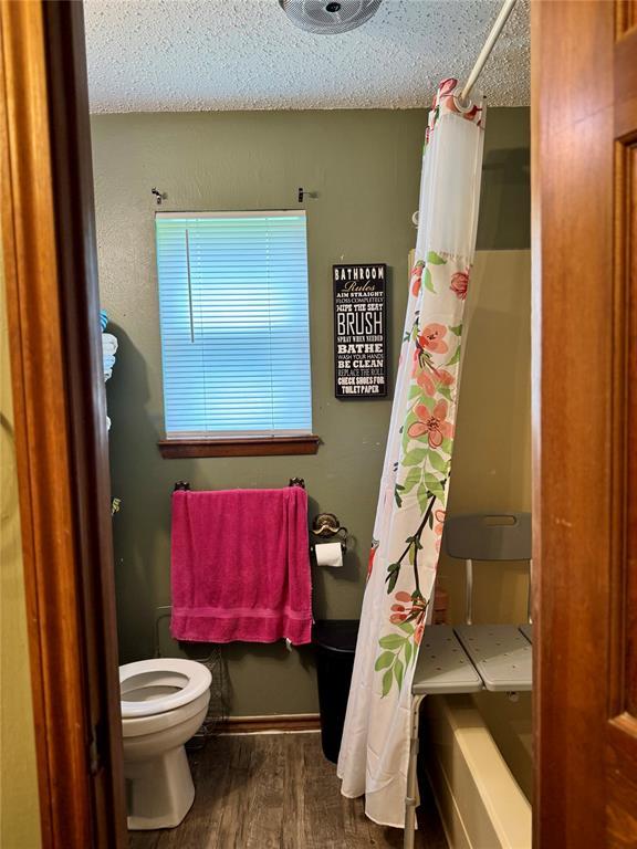 311 Parker St, Waurika, OK 73573 - bathroom with wood finished floors, shower / bath combo, and a textured ceiling