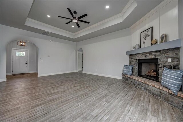 1890 E Industrial Rd, Guthrie, OK 73044 - unfurnished living room with arched walkways, a tray ceiling, crown molding, a ceiling fan, and a fireplace
