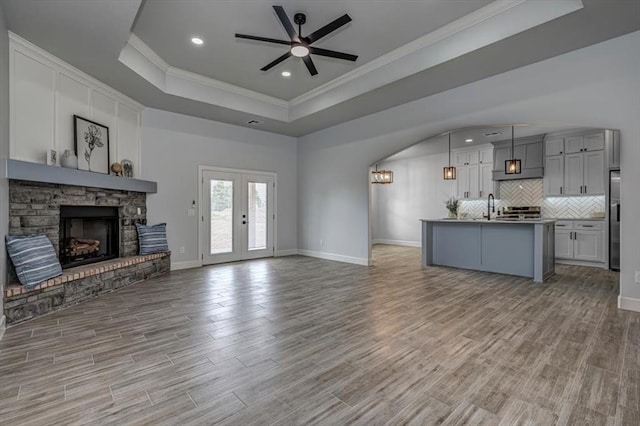 1890 E Industrial Rd, Guthrie, OK 73044 - unfurnished living room featuring a raised ceiling, ornamental molding, a ceiling fan, a fireplace, and light wood finished floors