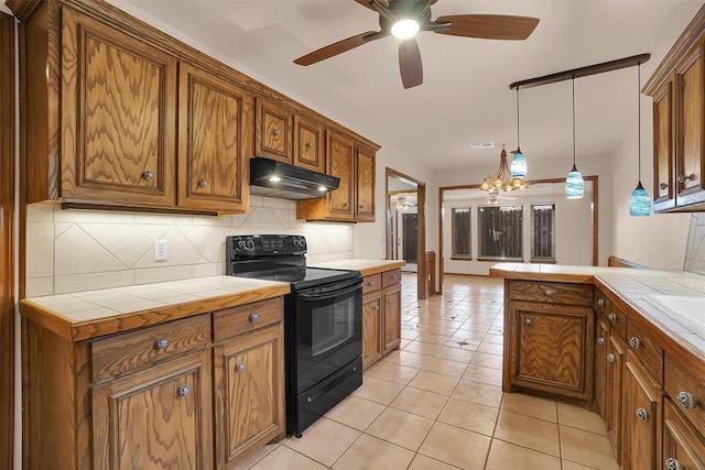 3217 Quail Cir, Altus, OK 73521 - kitchen with black range with electric stovetop, under cabinet range hood, tile counters, brown cabinetry, and decorative backsplash