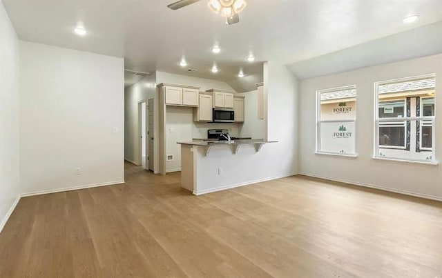 1426 SW Oklahoma Ave, Lawton, OK 73501 - kitchen featuring stainless steel microwave, a breakfast bar area, a peninsula, light wood finished floors, and vaulted ceiling