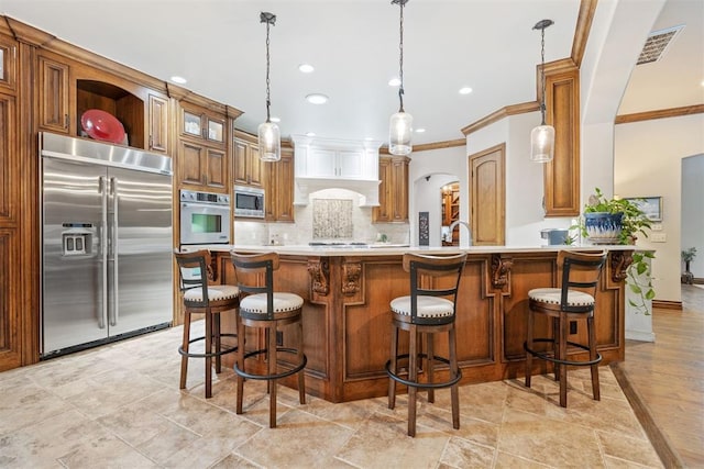 1605 Hidden Lake Dr, Edmond, OK 73034 - kitchen with built in appliances, brown cabinets, crown molding, backsplash, and a peninsula