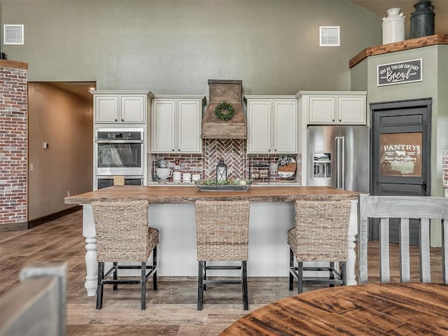 4920 W Forrest Hills Rd, Guthrie, OK 73044 - kitchen with custom range hood, stainless steel appliances, decorative backsplash, a towering ceiling, and a kitchen bar