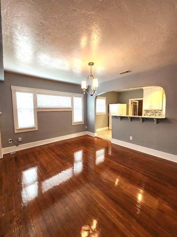2719 NW 14th St, Oklahoma City, OK 73107 - unfurnished living room with hardwood / wood-style floors, a chandelier, arched walkways, and a textured ceiling
