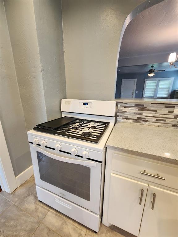 2719 NW 14th St, Oklahoma City, OK 73107 - kitchen with white range with gas stovetop, white cabinetry, a textured wall, a ceiling fan, and light stone countertops