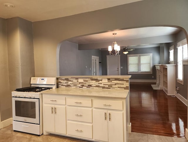 2719 NW 14th St, Oklahoma City, OK 73107 - kitchen with white gas stove, arched walkways, white cabinets, and hanging light fixtures