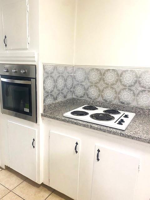 6101 S Douglas Ave, Oklahoma City, OK 73139 - kitchen with oven, white electric cooktop, light tile patterned flooring, white cabinets, and decorative backsplash