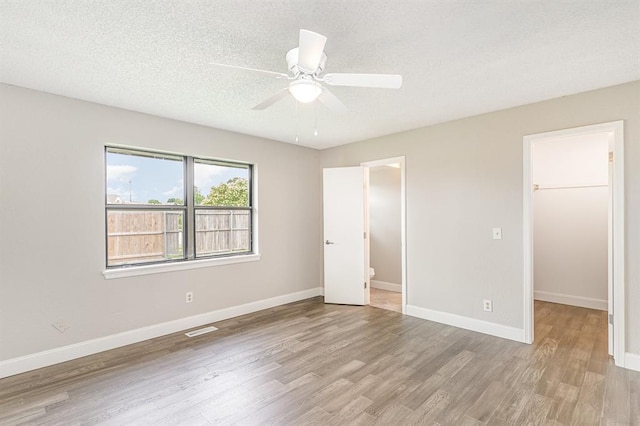 1004 Ranchoak Ct, Yukon, OK 73099 - unfurnished bedroom featuring wood finished floors, a walk in closet, a textured ceiling, a closet, and ceiling fan