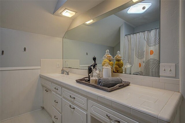 4973 NW 31st Ter, Oklahoma City, OK 73122 - bathroom featuring double vanity, vaulted ceiling, and a wainscoted wall
