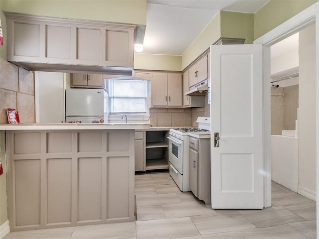 312 NW 24th St, Oklahoma City, OK 73103 - kitchen with white appliances, under cabinet range hood, light countertops, and decorative backsplash