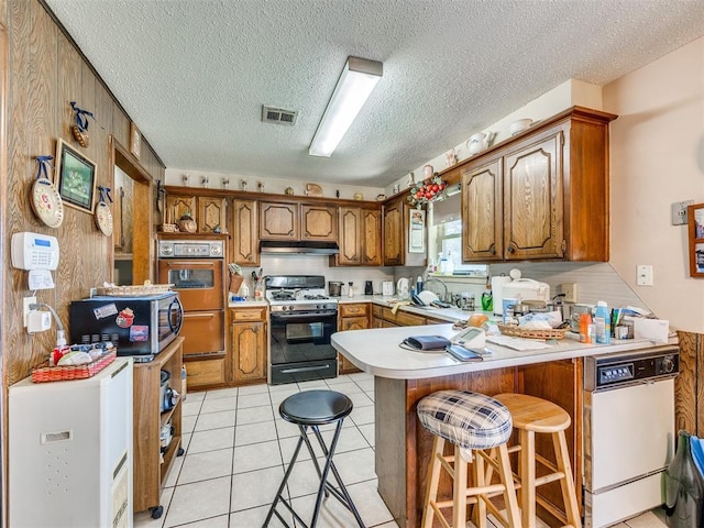 4021 E Larkwood Dr, Del City, OK 73115 - kitchen featuring range with gas stovetop, oven, under cabinet range hood, a peninsula, and stainless steel microwave