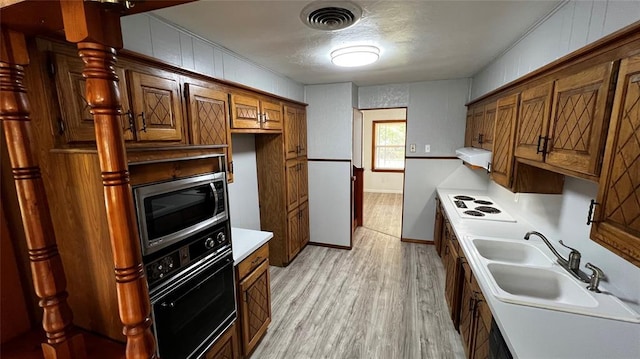 425 Mohawk Dr, Pauls Valley, OK 73075 - kitchen featuring stainless steel microwave, white electric cooktop, light wood finished floors, extractor fan, and brown cabinets