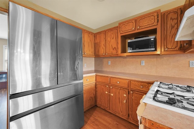 231 W Polk St, Mangum, OK 73554 - kitchen with stainless steel appliances, under cabinet range hood, light countertops, backsplash, and brown cabinets