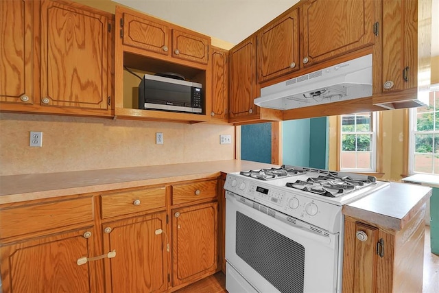 231 W Polk St, Mangum, OK 73554 - kitchen with white gas range, under cabinet range hood, stainless steel microwave, a peninsula, and light countertops
