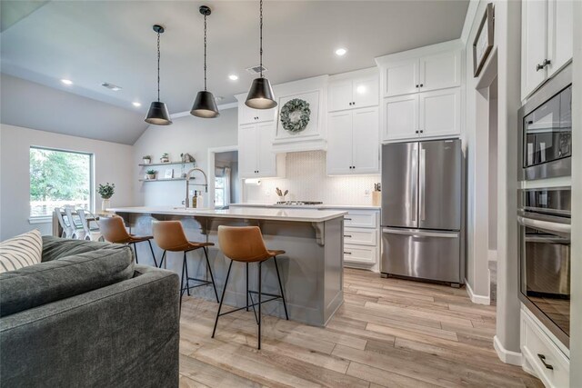 13420 Saltgrass Dr, Edmond, OK 73025 - kitchen featuring appliances with stainless steel finishes, light countertops, a kitchen bar, backsplash, and light wood finished floors