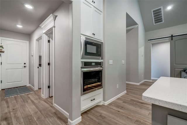 13420 Saltgrass Dr, Edmond, OK 73025 - kitchen featuring oven, black microwave, a barn door, light wood-style floors, and white cabinets