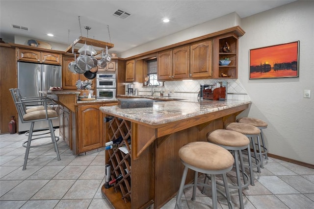 2205 SE 90th St, Lawton, OK 73501 - kitchen with brown cabinets, tasteful backsplash, appliances with stainless steel finishes, light stone counters, and open shelves