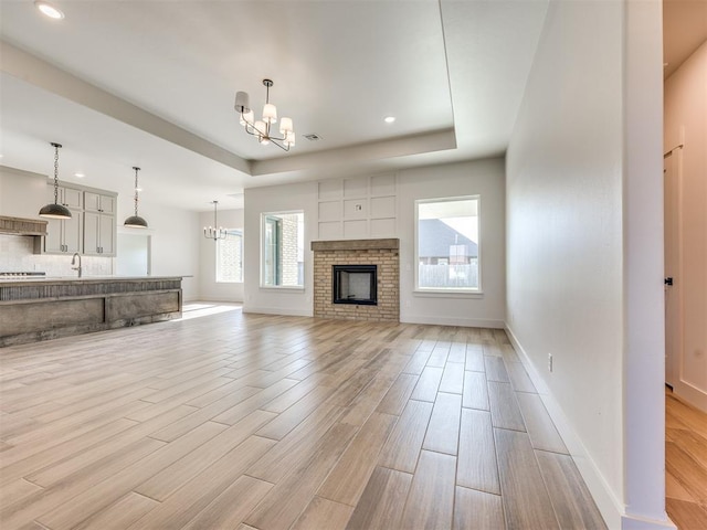 1136 Jozie Way, Tuttle, OK 73089 - unfurnished living room with a chandelier, a raised ceiling, light wood-type flooring, a fireplace, and recessed lighting