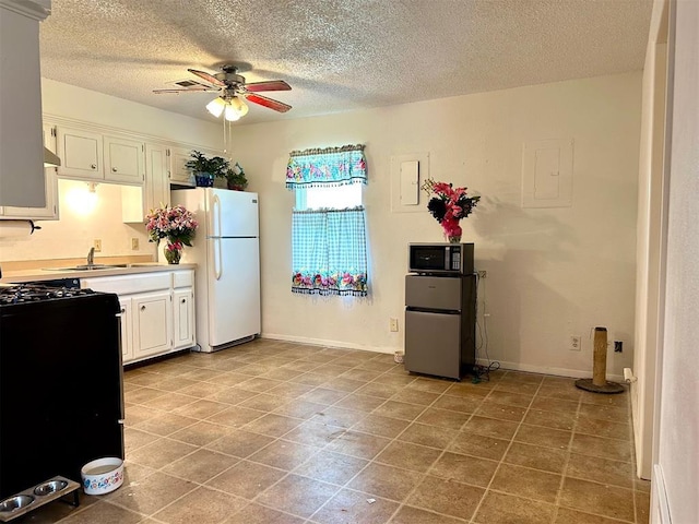 909 N Center St, Shawnee, OK 74801 - kitchen featuring stove, freestanding refrigerator, a ceiling fan, a textured ceiling, and white cabinetry