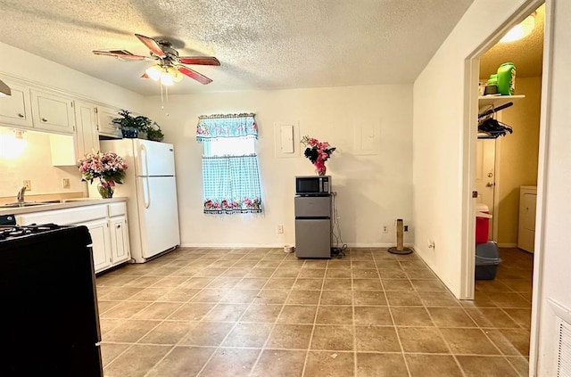 909 N Center St, Shawnee, OK 74801 - kitchen with range, ceiling fan, freestanding refrigerator, a textured ceiling, and white cabinetry