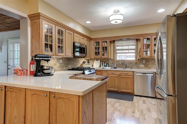 1825 Kings Rd, Edmond, OK 73013 - kitchen with appliances with stainless steel finishes, a peninsula, light wood finished floors, tasteful backsplash, and light countertops