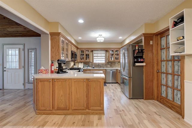 1825 Kings Rd, Edmond, OK 73013 - kitchen featuring appliances with stainless steel finishes, a peninsula, light wood-type flooring, light countertops, and backsplash