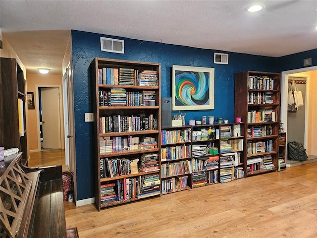 3205 NW 62nd St, Oklahoma City, OK 73112 - living area featuring a textured wall, wood finished floors, wall of books, and a textured ceiling