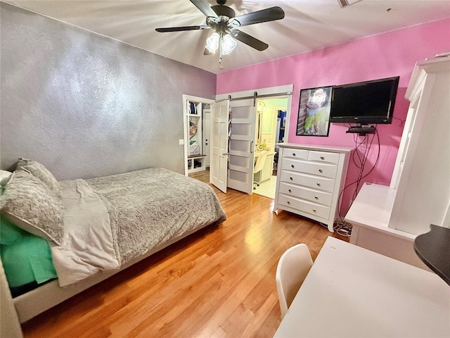 1118 Fernwood Dr, Midwest City, OK 73130 - bedroom featuring a barn door, wood finished floors, a ceiling fan, and connected bathroom