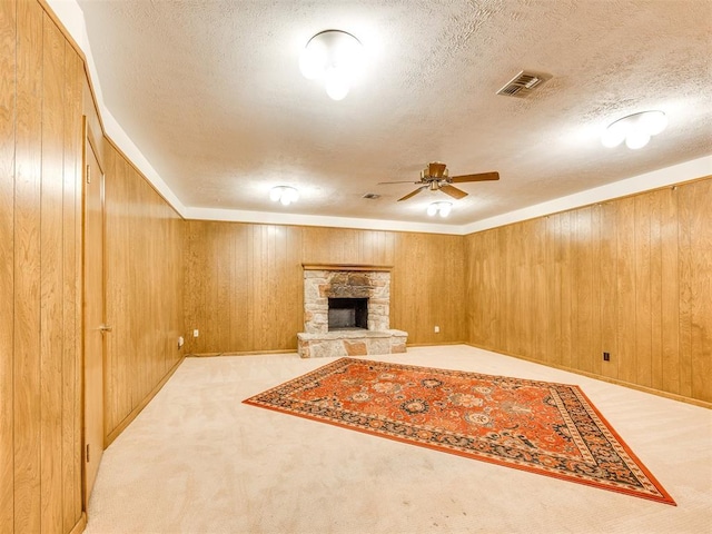 7600 NW 27th St, Bethany, OK 73008 - unfurnished living room with a textured ceiling, a ceiling fan, wooden walls, carpet floors, and a stone fireplace