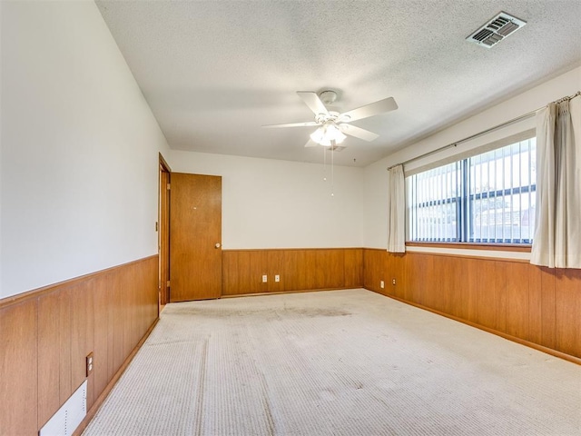 7600 NW 27th St, Bethany, OK 73008 - empty room with wood walls, a wainscoted wall, ceiling fan, a textured ceiling, and light carpet