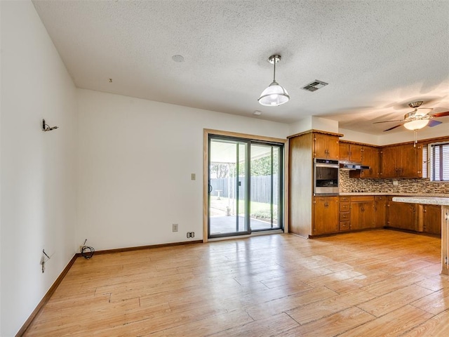 7600 NW 27th St, Bethany, OK 73008 - kitchen featuring stainless steel oven, brown cabinets, backsplash, light wood-style floors, and a textured ceiling